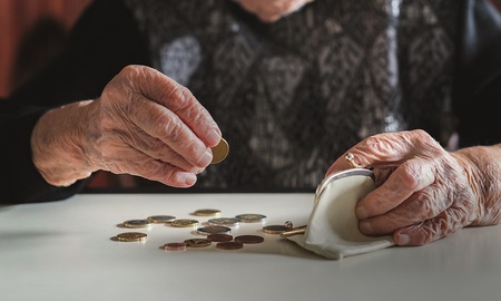 Elderly 95 years old woman sitting miserably at the table at home and counting remaining coins from the pension in her wallet after paying the bills.